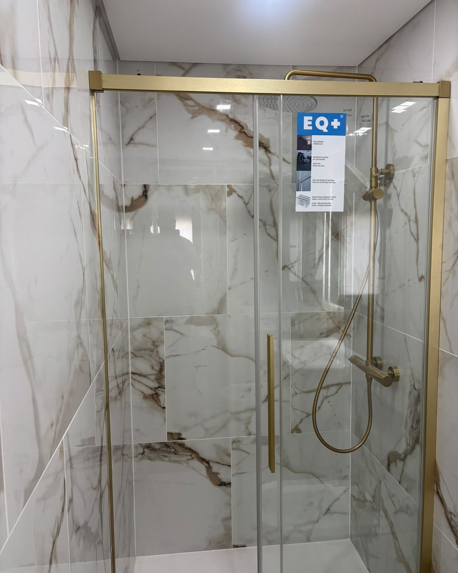 Base de duche com resguardo de vidro de perfis dourados e chuveiro dourado