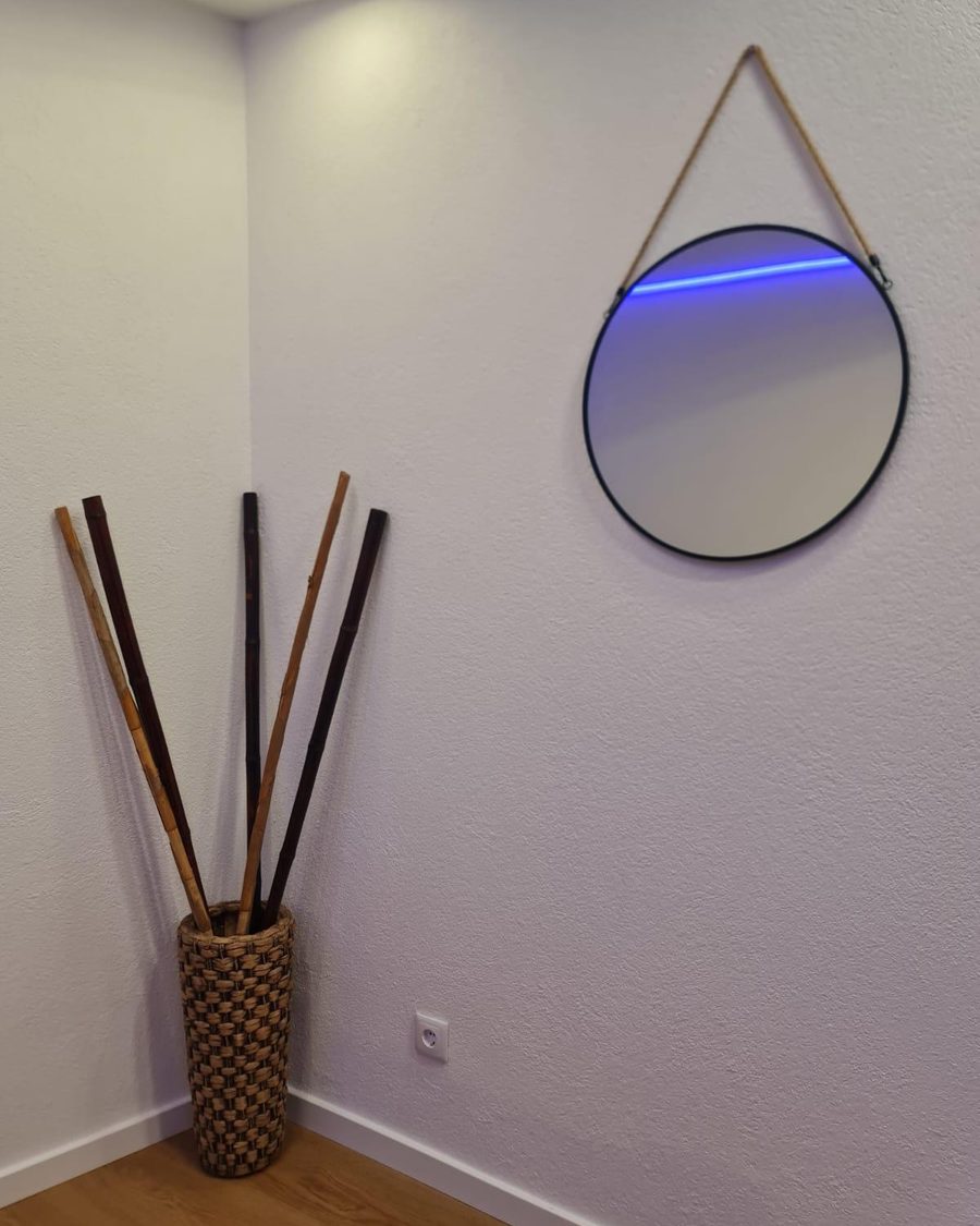 Canto do escritório com espelho redondo iluminado por LED e jarra decorativa