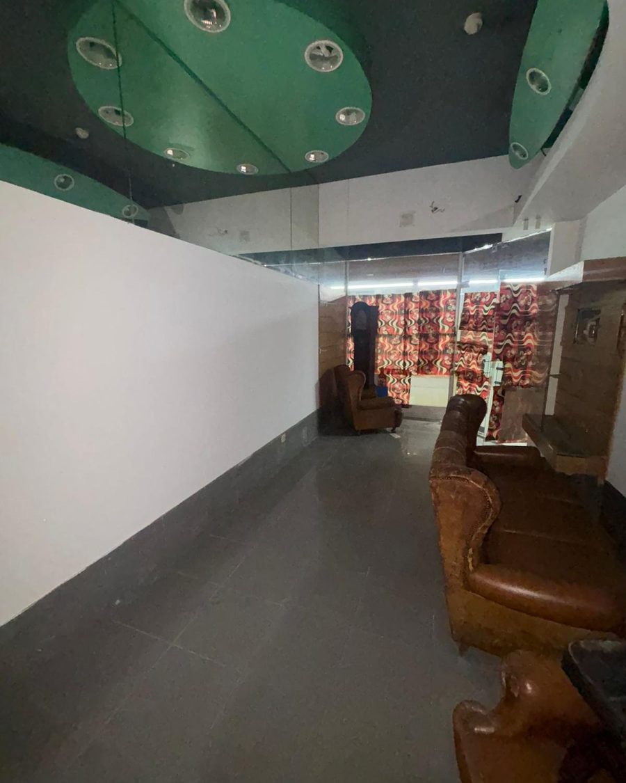 Espaço comercial antes da obra, com teto rebaixado verde, pavimento escuro e poltronas antigas