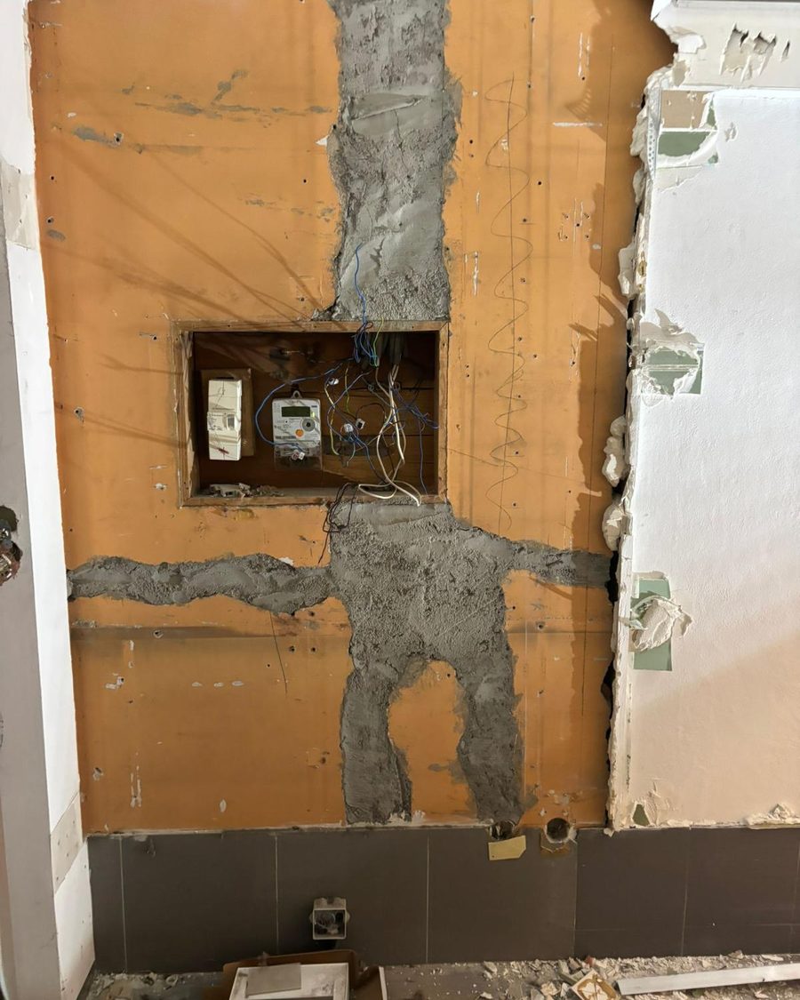 Parede forrada a madeira aberta durante a obra, com os roços e a caixa do contador à vista