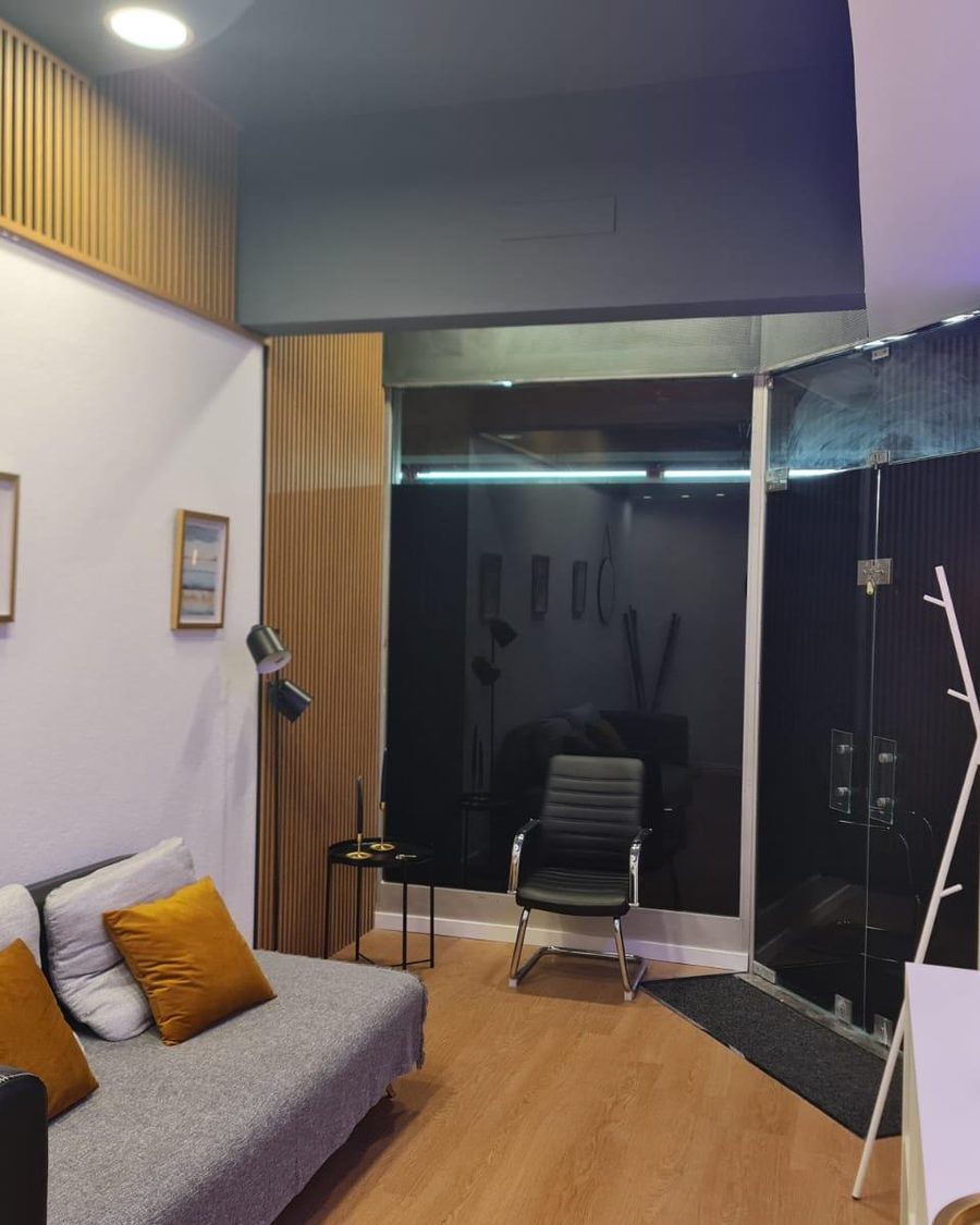 Zona de estar do escritório com sofá, ripado de madeira e a entrada envidraçada ao fundo