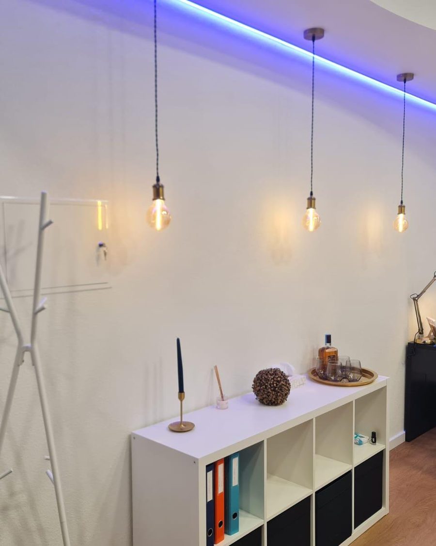 Parede com candeeiros suspensos, perfil de LED no teto, estante e secretária