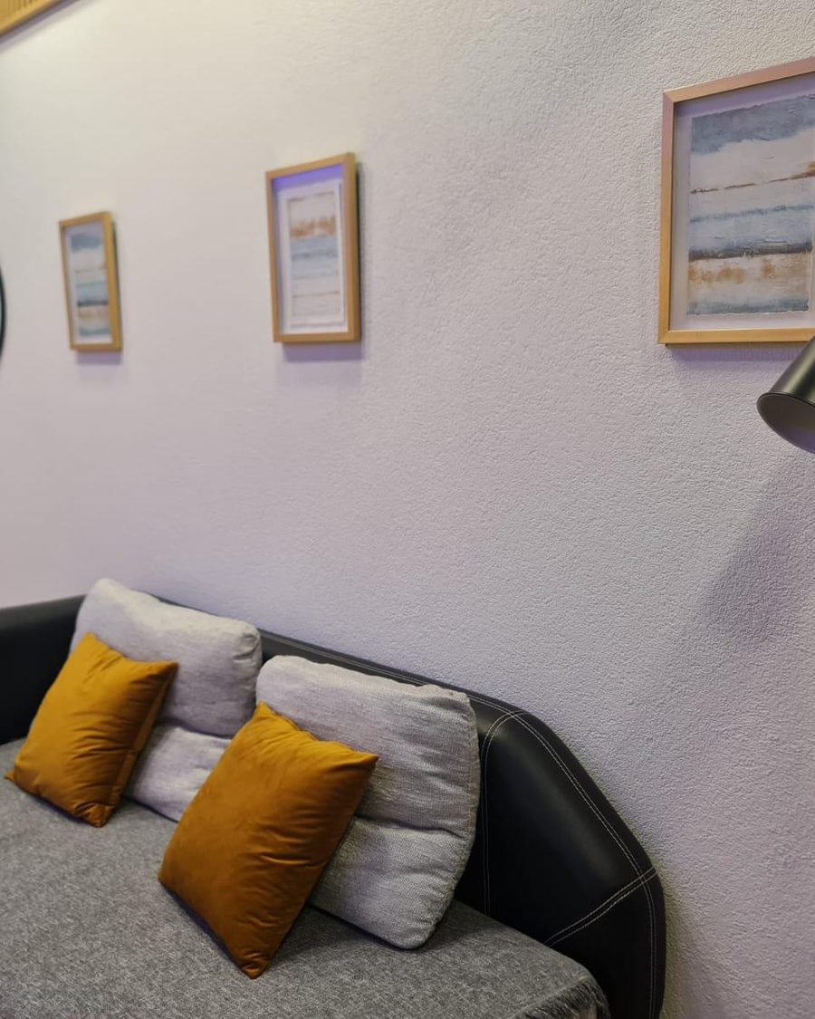 Parede pintada de branco com quadros, sofá e candeeiro de pé