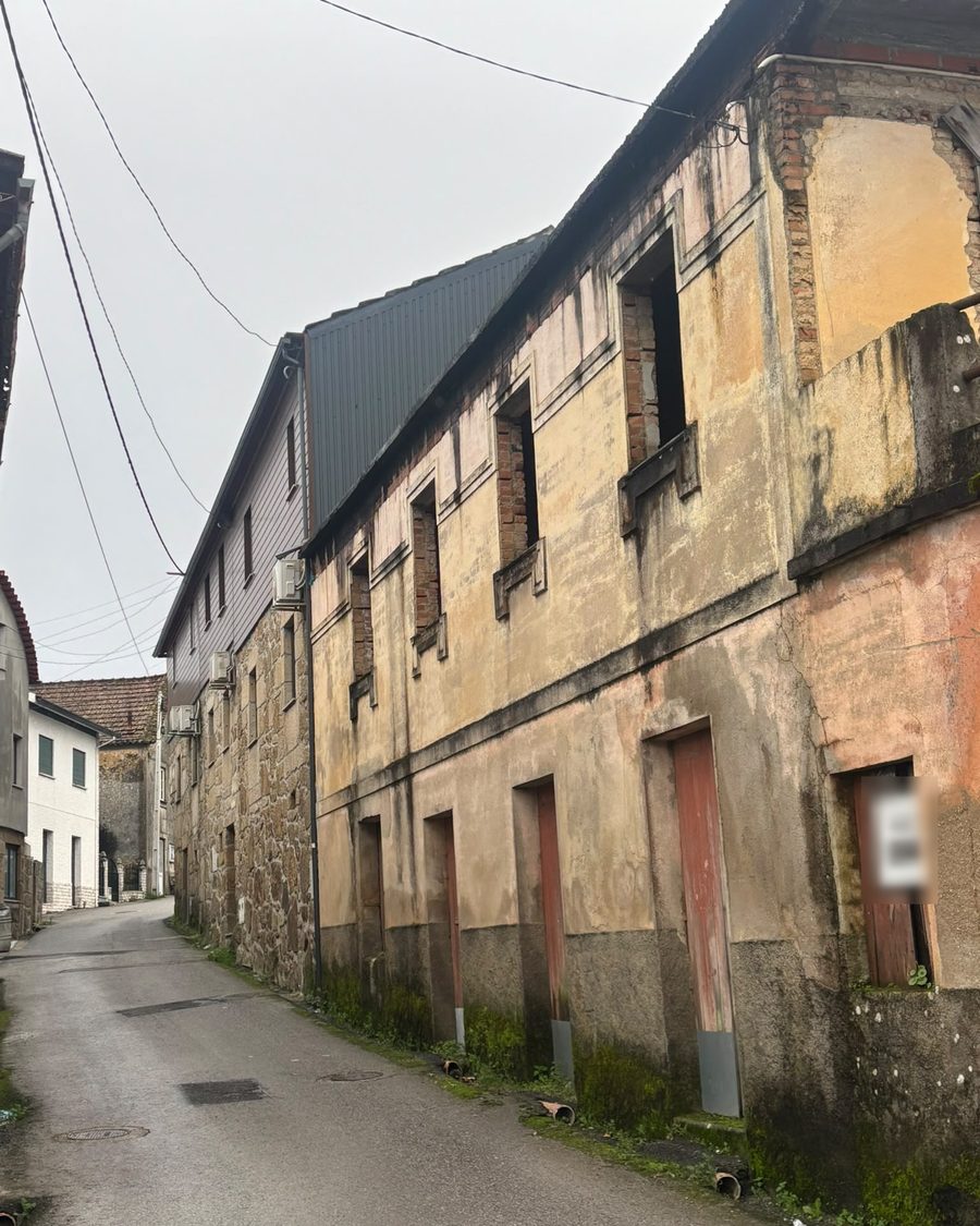 Casa de dois pisos antes da obra, com o reboco velho e manchado numa rua estreita