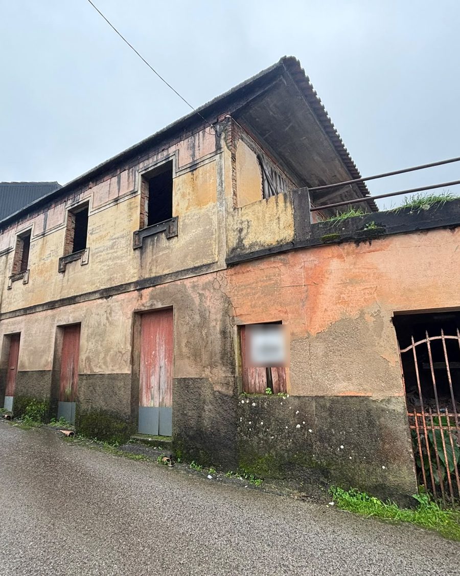 Fachada gasta de uma casa de dois pisos, com um portão de ferro ao lado