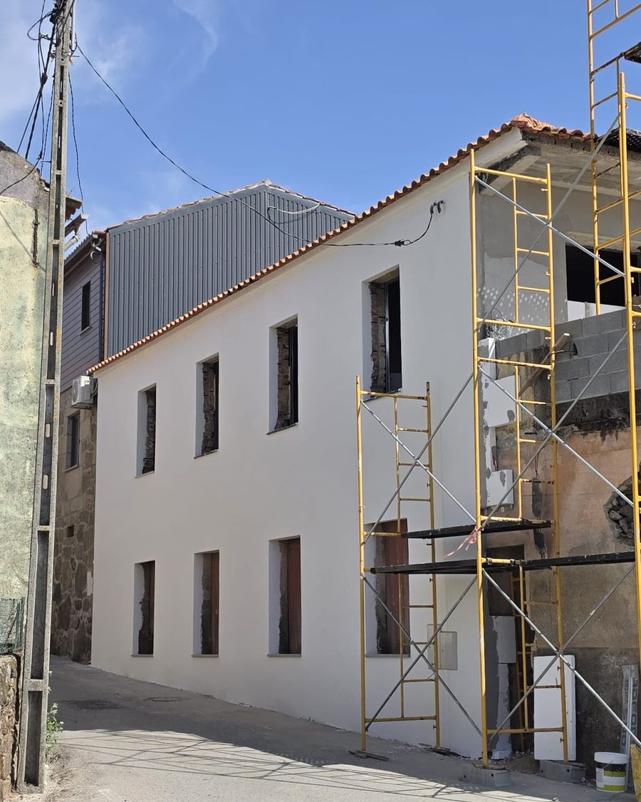 Casa de dois pisos pintada de branco vista da rua, ainda com um andaime ao lado