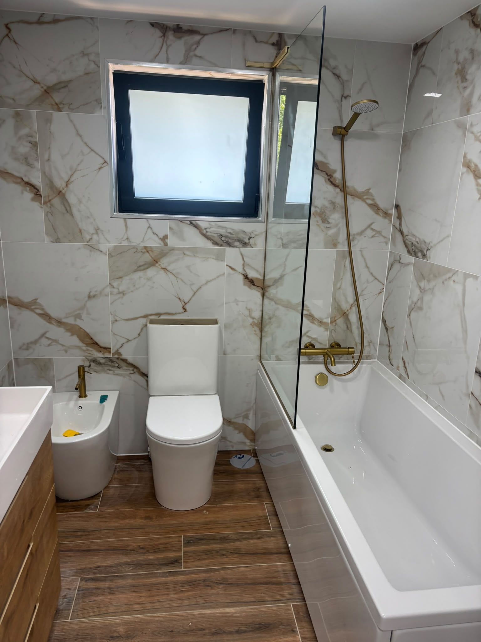 Casa de banho remodelada com revestimento efeito mármore, banheira com resguardo de vidro, bidé e sanita