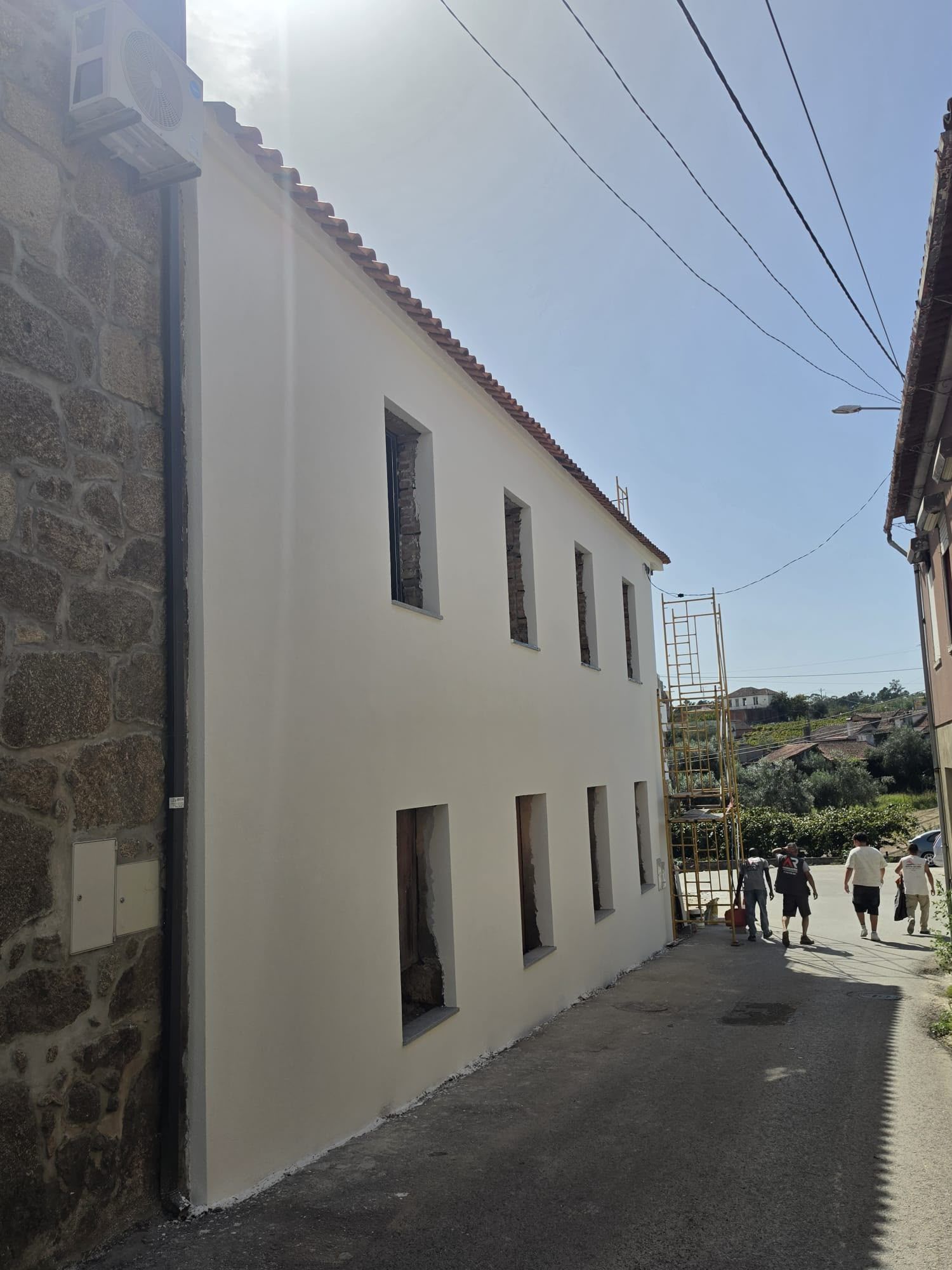 Casa de dois pisos com a fachada isolada e pintada de branco numa rua estreita