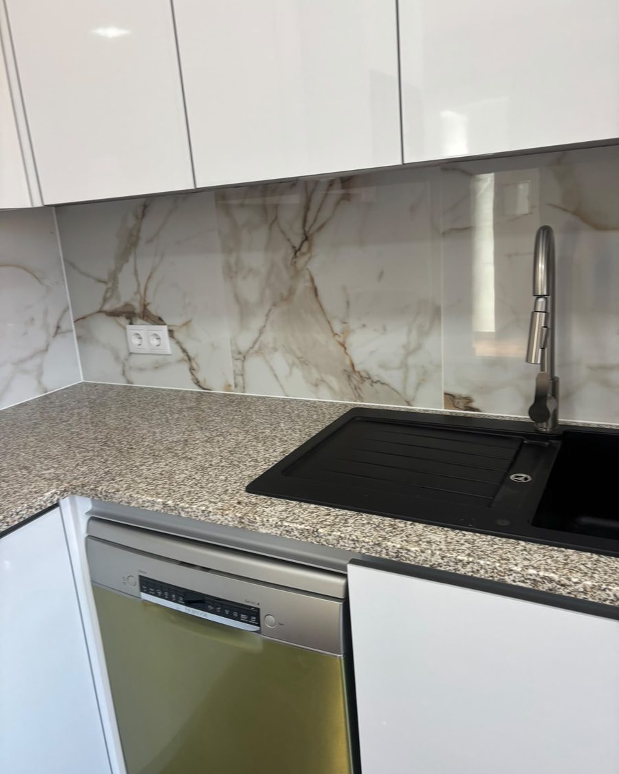 Cozinha com móveis brancos lacados, revestimento efeito mármore e lava-loiça preto