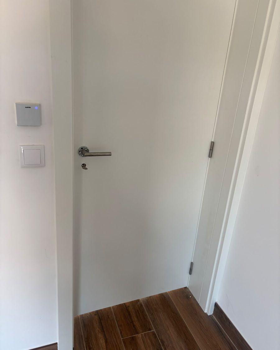 Porta interior lacada a branco com puxador de inox sobre pavimento efeito madeira