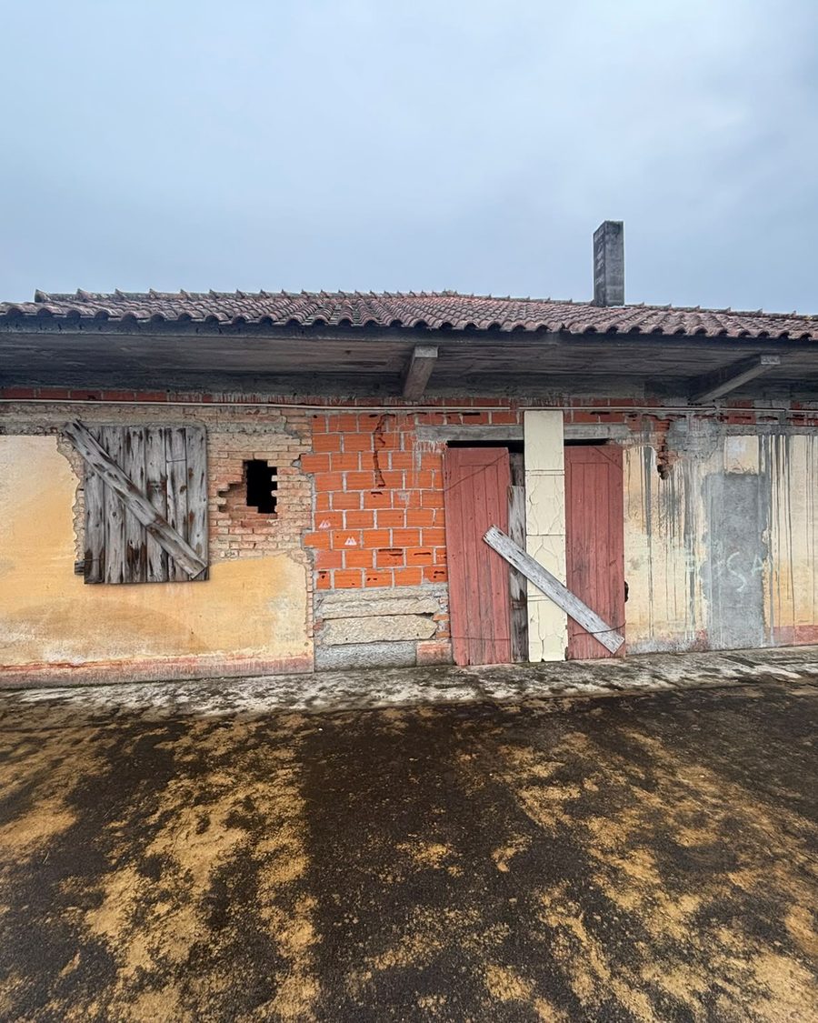 Frente da moradia antes da obra, com janelas tapadas a madeira e paredes descascadas