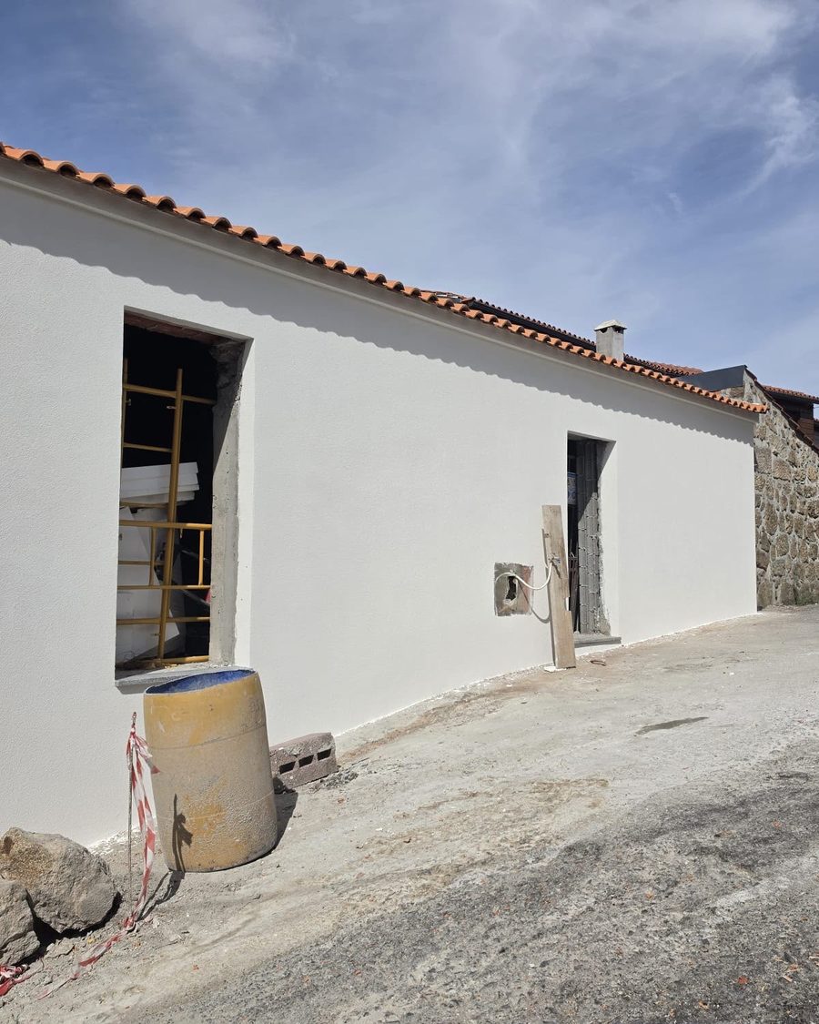 Fachada lateral da moradia pintada de branco, numa rua de aldeia